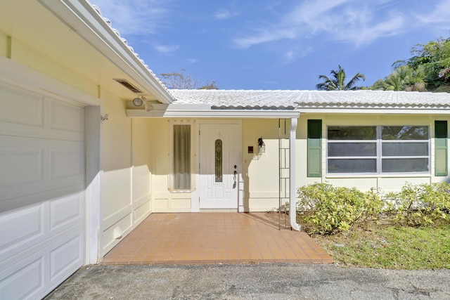 entrance to property with a garage, stucco siding, visible vents, and a tiled roof