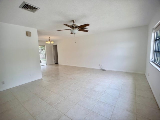 empty room featuring light tile patterned floors, a textured ceiling, ceiling fan with notable chandelier, visible vents, and baseboards