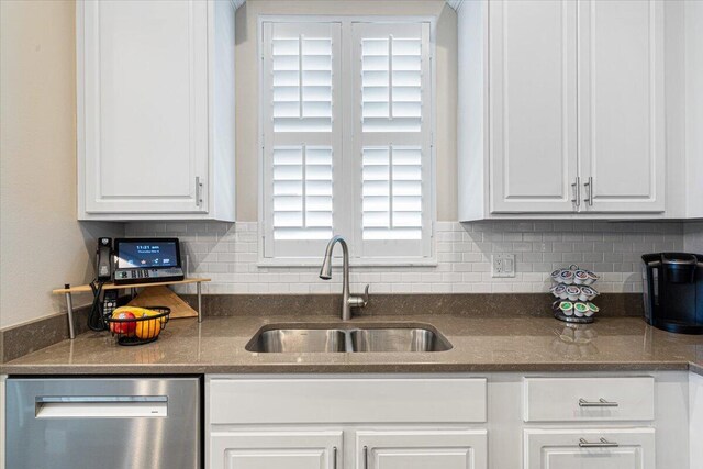 kitchen with tasteful backsplash, dishwasher, dark stone countertops, white cabinetry, and a sink