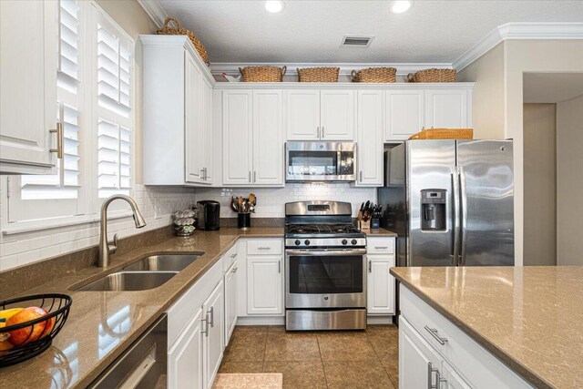 kitchen featuring appliances with stainless steel finishes, white cabinets, a sink, and ornamental molding