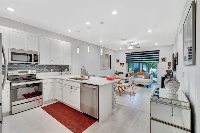 kitchen with a sink, backsplash, open floor plan, appliances with stainless steel finishes, and light countertops