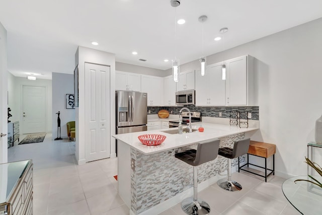 kitchen with backsplash, a kitchen breakfast bar, appliances with stainless steel finishes, a peninsula, and a sink