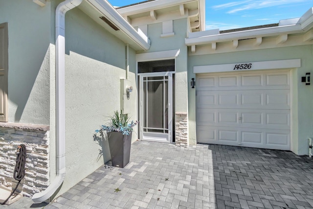 view of exterior entry with stone siding, stucco siding, decorative driveway, and a garage