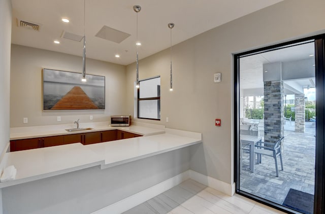 kitchen with visible vents, pendant lighting, a sink, light countertops, and baseboards