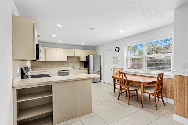 kitchen with cream cabinetry, stainless steel appliances, light countertops, a sink, and a peninsula