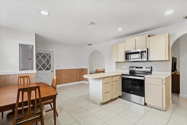 kitchen featuring a wainscoted wall, stainless steel appliances, light countertops, electric panel, and a peninsula