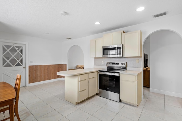 kitchen featuring cream cabinets, stainless steel appliances, a peninsula, visible vents, and light countertops