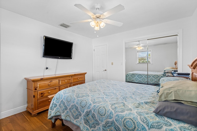 bedroom featuring ceiling fan, wood finished floors, visible vents, baseboards, and a closet