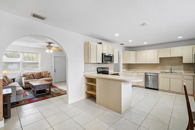 kitchen with arched walkways, a sink, visible vents, open floor plan, and appliances with stainless steel finishes