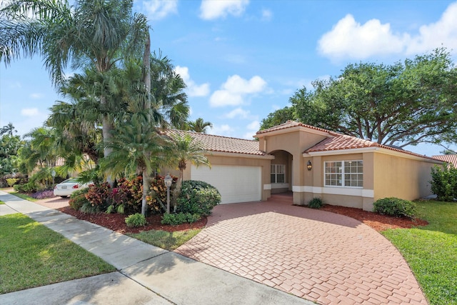 mediterranean / spanish house with a garage, decorative driveway, a tiled roof, and stucco siding