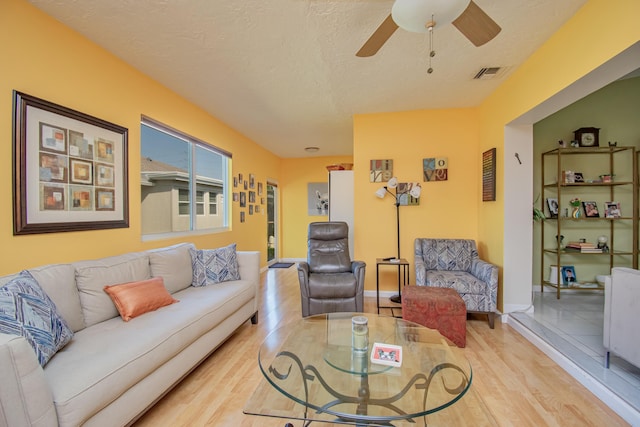 living room with visible vents, a textured ceiling, ceiling fan, and light wood finished floors