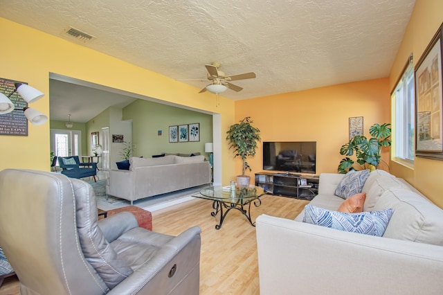 living room featuring a textured ceiling, light wood-style flooring, visible vents, and ceiling fan