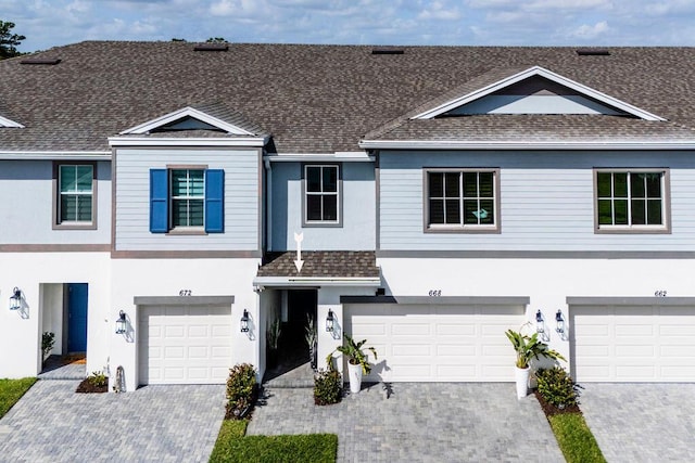 multi unit property featuring roof with shingles, driveway, an attached garage, and stucco siding