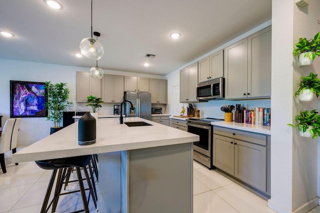 kitchen featuring appliances with stainless steel finishes, gray cabinets, light countertops, a kitchen bar, and a sink