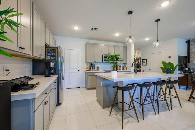 kitchen with light countertops, visible vents, gray cabinetry, a sink, and a kitchen bar