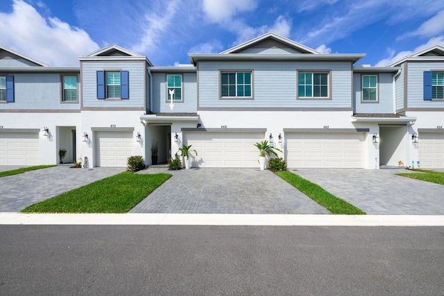 townhome / multi-family property with a garage, decorative driveway, and stucco siding