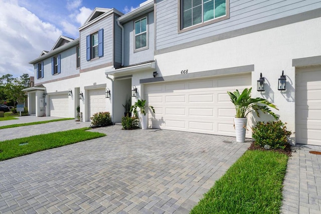 townhome / multi-family property with a garage, decorative driveway, and stucco siding