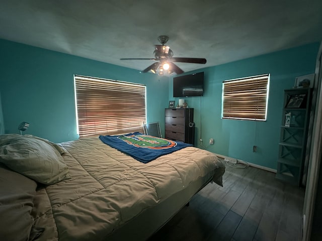 bedroom featuring ceiling fan, multiple windows, baseboards, and wood finished floors