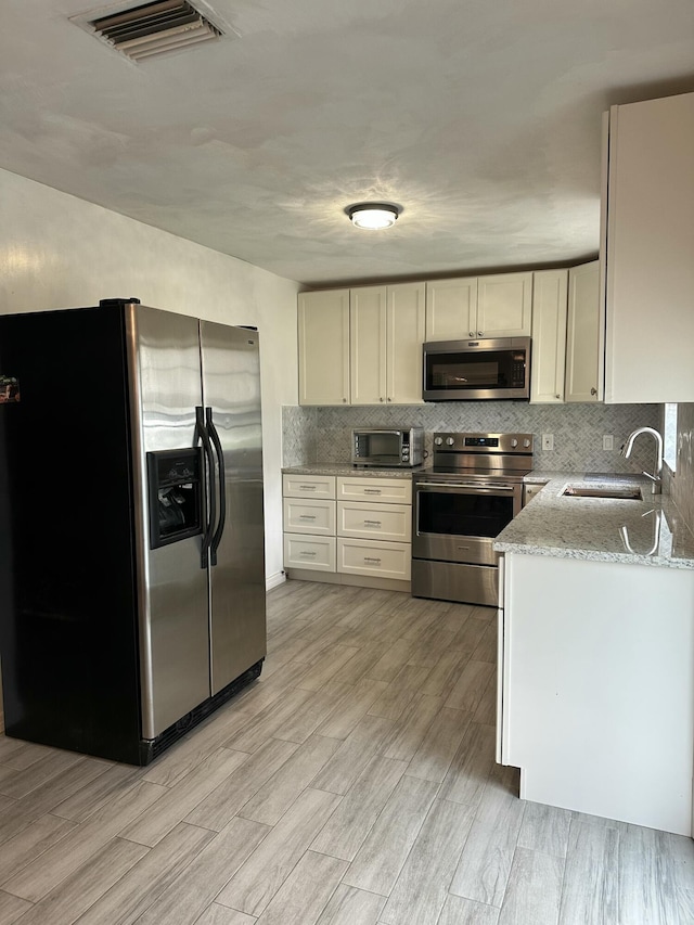 kitchen featuring light stone counters, stainless steel appliances, a sink, visible vents, and tasteful backsplash