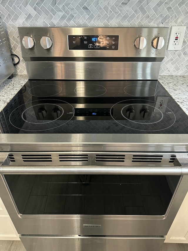 interior details with tasteful backsplash, stainless steel electric range, and light countertops