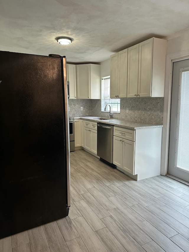 kitchen with decorative backsplash, appliances with stainless steel finishes, wood tiled floor, white cabinetry, and a sink