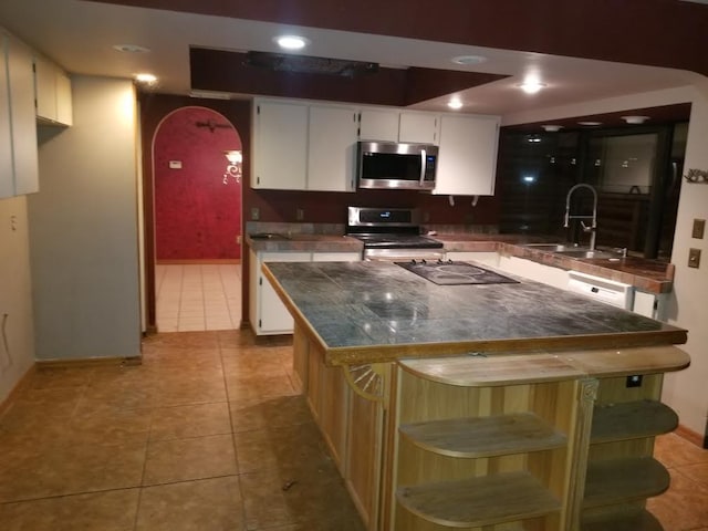 kitchen with light tile patterned floors, a kitchen island, appliances with stainless steel finishes, and a sink