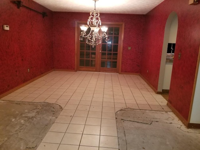 unfurnished dining area featuring arched walkways, light tile patterned floors, a chandelier, baseboards, and wallpapered walls