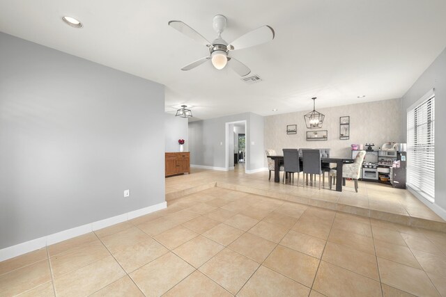 unfurnished dining area featuring ceiling fan with notable chandelier, visible vents, baseboards, and light tile patterned flooring