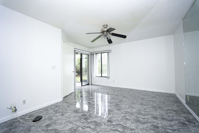 empty room with a textured ceiling, ceiling fan, marble finish floor, and baseboards