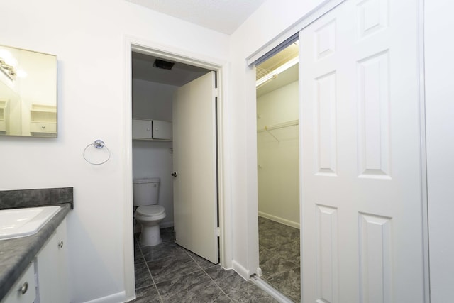 bathroom featuring toilet, visible vents, baseboards, vanity, and a walk in closet