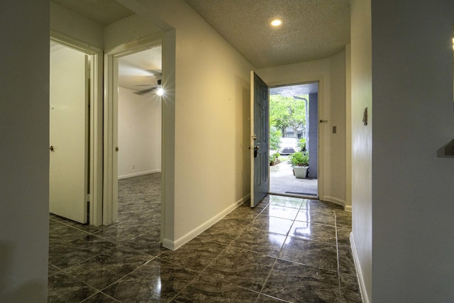 corridor with a textured ceiling, marble finish floor, and baseboards