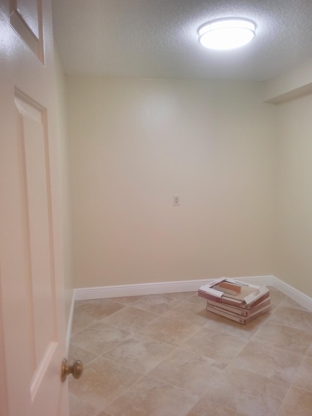 empty room featuring light tile patterned floors, baseboards, and a textured ceiling