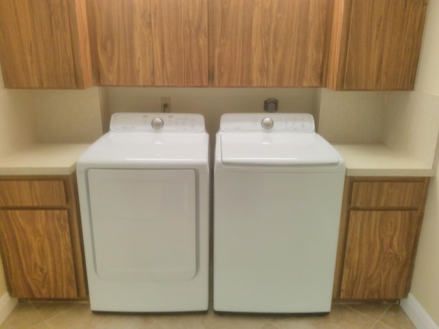 clothes washing area featuring washer and dryer, light tile patterned floors, and cabinet space