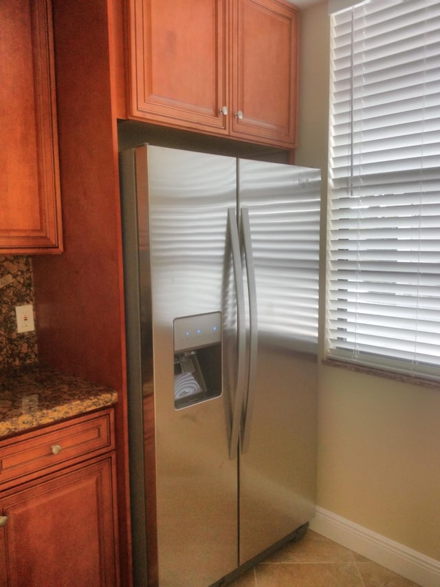 kitchen featuring backsplash, baseboards, light tile patterned floors, dark stone countertops, and stainless steel refrigerator with ice dispenser