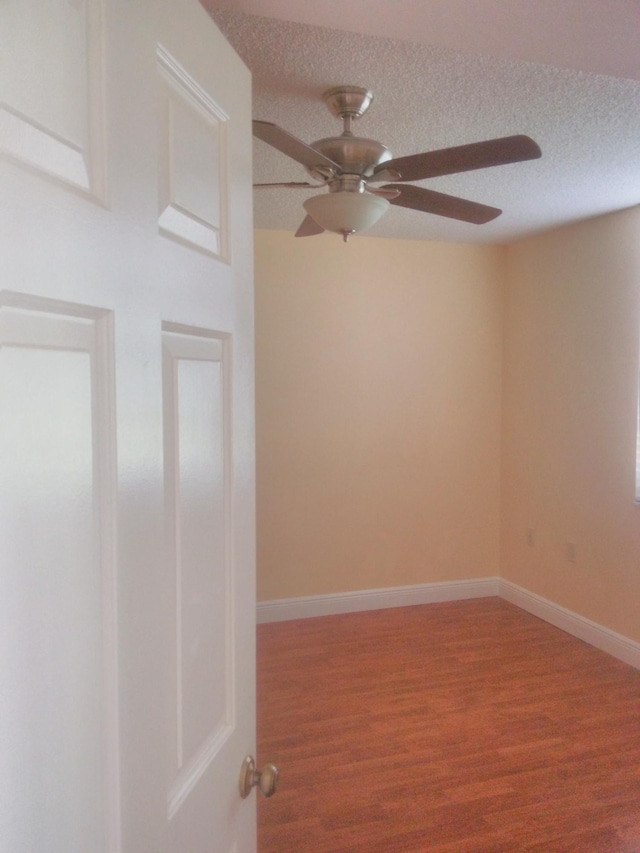 unfurnished room with ceiling fan, wood finished floors, baseboards, and a textured ceiling