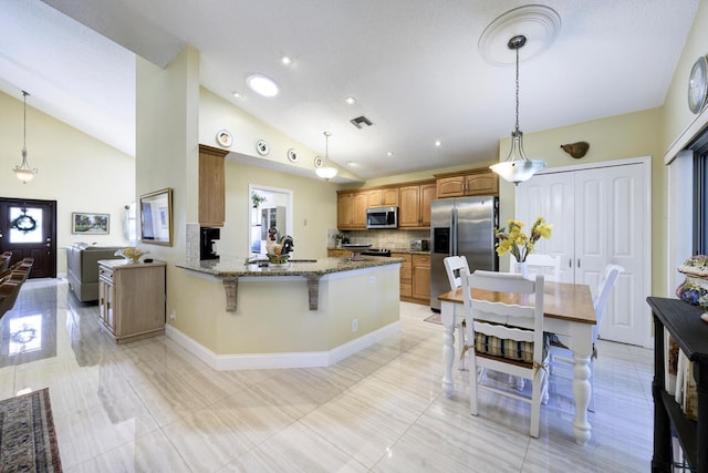 kitchen with a peninsula, visible vents, appliances with stainless steel finishes, brown cabinetry, and dark stone countertops