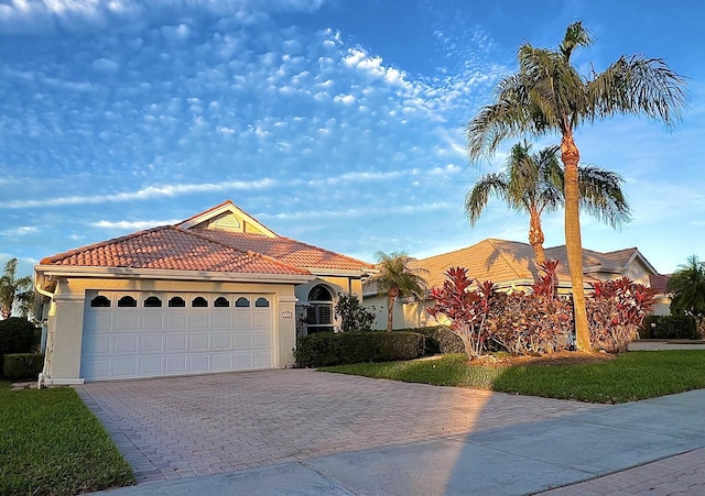 mediterranean / spanish-style home featuring a garage, decorative driveway, a tiled roof, and stucco siding