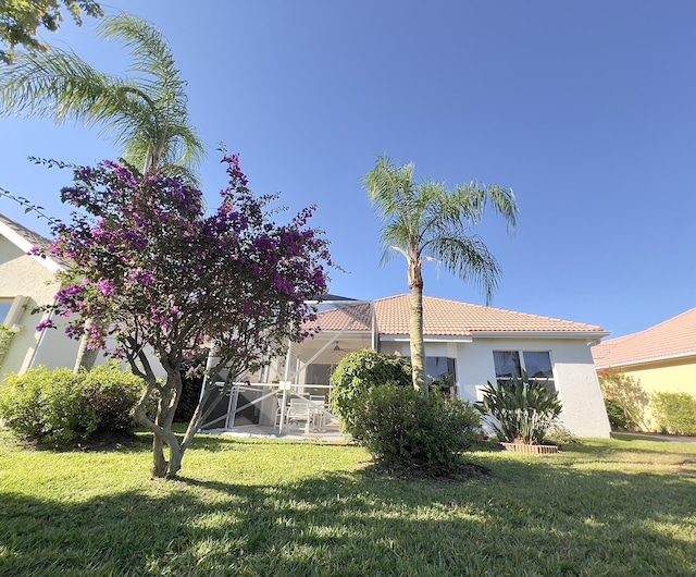 back of property featuring a lawn, glass enclosure, stucco siding, and a tiled roof