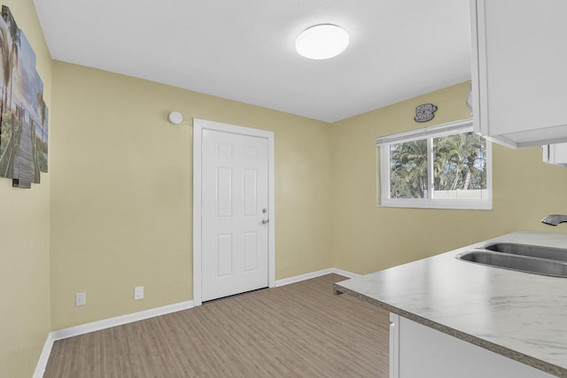 kitchen with light wood-style floors, baseboards, white cabinets, and a sink