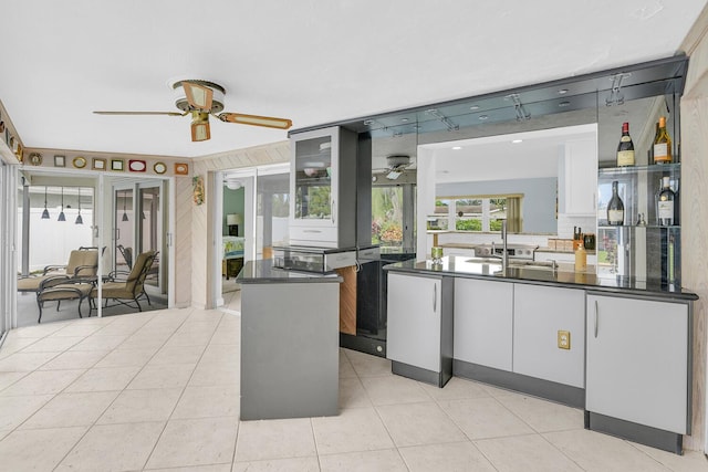 kitchen featuring light tile patterned floors, dark countertops, ceiling fan, a sink, and a peninsula