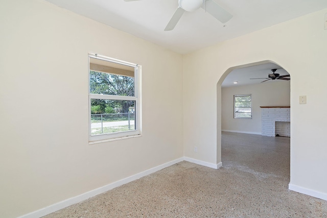 unfurnished room with arched walkways, a brick fireplace, baseboards, and speckled floor