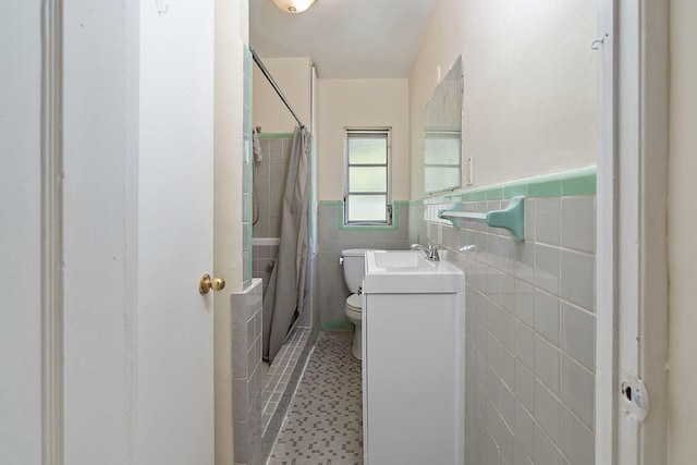 bathroom with tile walls, toilet, a wainscoted wall, tile patterned floors, and a sink