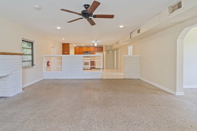 unfurnished living room with baseboards, visible vents, a ceiling fan, arched walkways, and light speckled floor