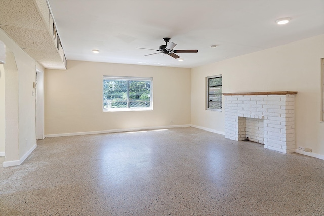 unfurnished living room with a fireplace, baseboards, a ceiling fan, and speckled floor