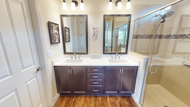 bathroom with a stall shower, double vanity, a sink, and wood finished floors