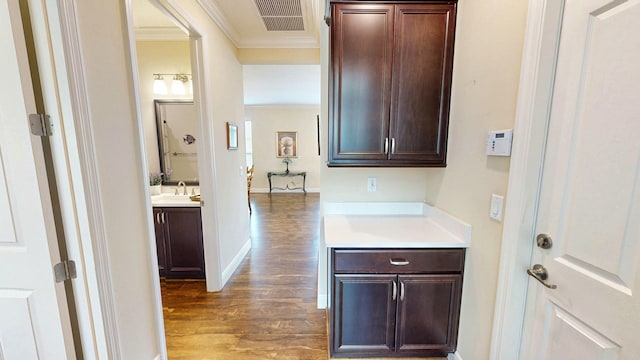 interior space featuring baseboards, visible vents, ornamental molding, wood finished floors, and a sink