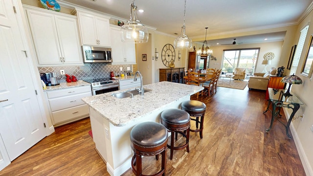 kitchen with crown molding, decorative backsplash, appliances with stainless steel finishes, a kitchen island with sink, and a sink