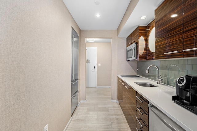 kitchen with tasteful backsplash, modern cabinets, stainless steel appliances, light countertops, and a sink