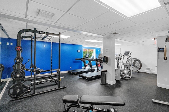 exercise room with a paneled ceiling, visible vents, and baseboards