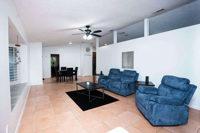 living room featuring vaulted ceiling, light tile patterned floors, a ceiling fan, a textured ceiling, and baseboards